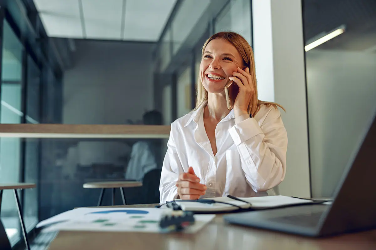 Glad kvinna i vit skjorta pratar i telefon