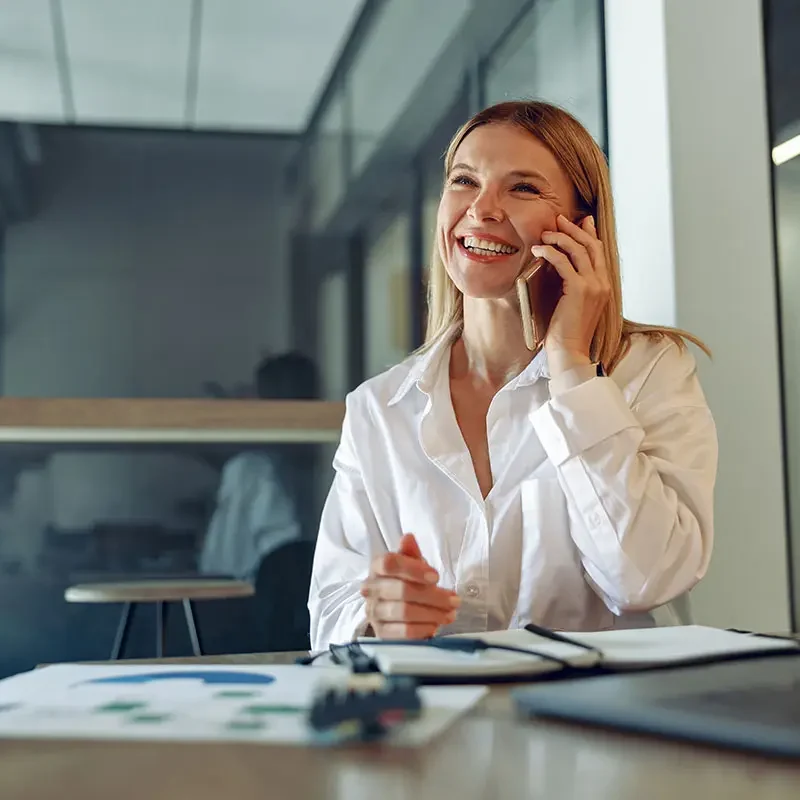 Glad kvinna i vit skjorta pratar i telefon