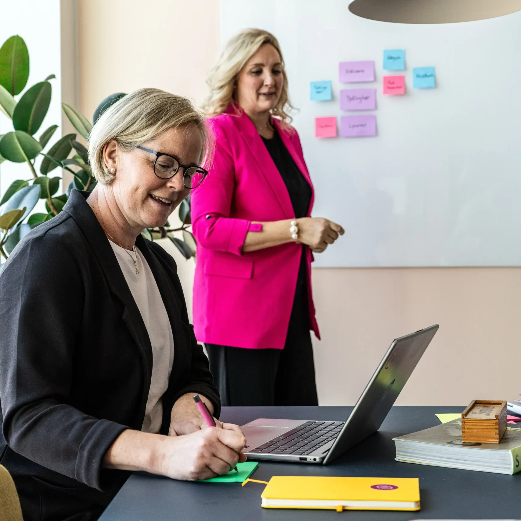 Anki på Inspirea skriver på en grön postit-lapp medans Jessica står i bakgrunden och tittar på